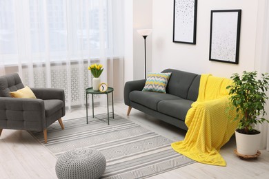 Photo of Spring atmosphere. Stylish living room interior with comfortable furniture and bouquet of beautiful yellow tulips