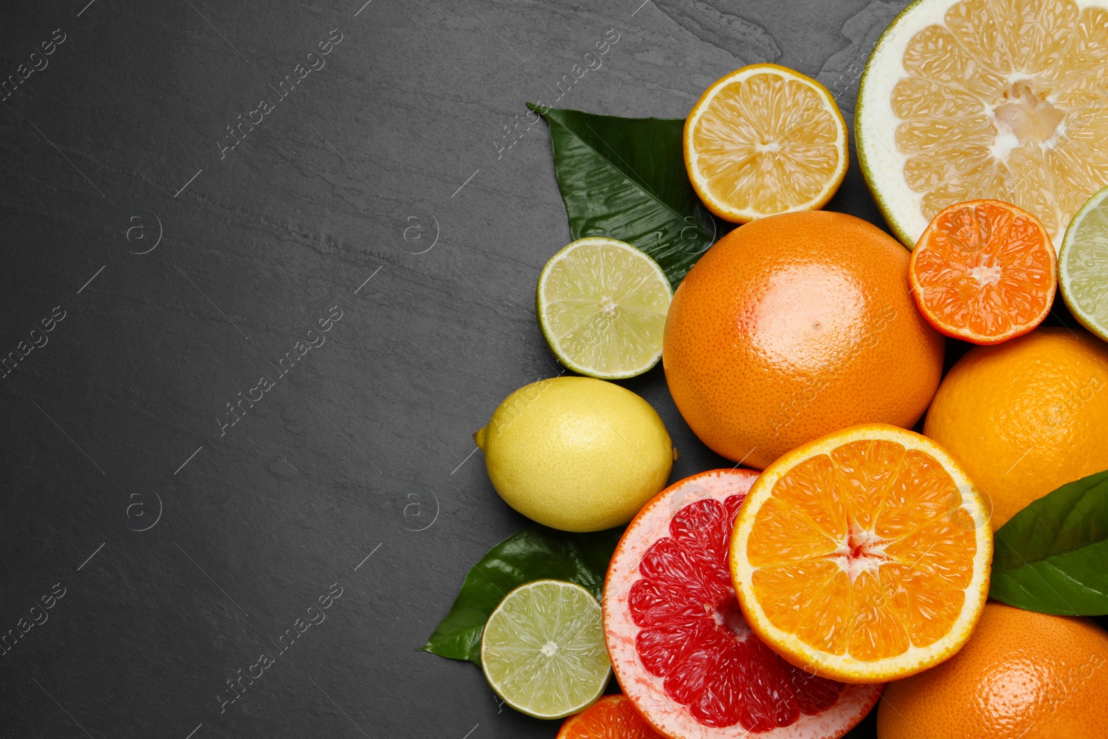 Photo of Different ripe citrus fruits with green leaves on black table, flat lay. Space for text