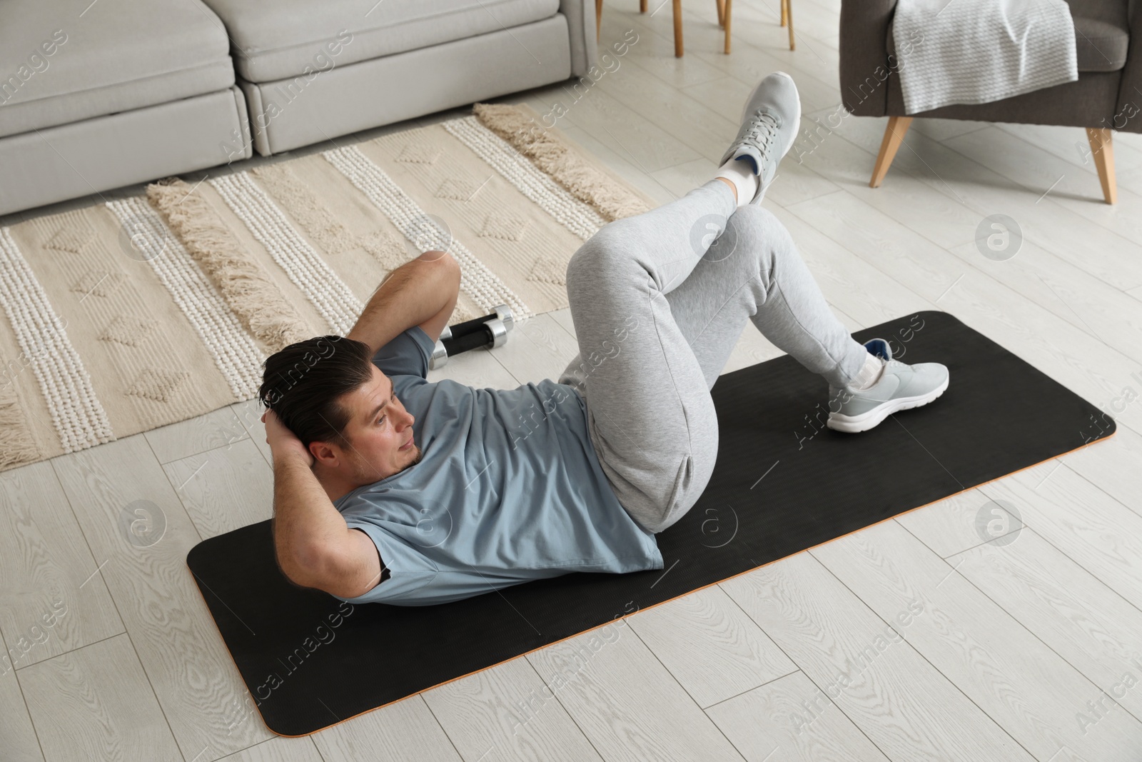 Photo of Overweight man doing abs exercise on mat at home
