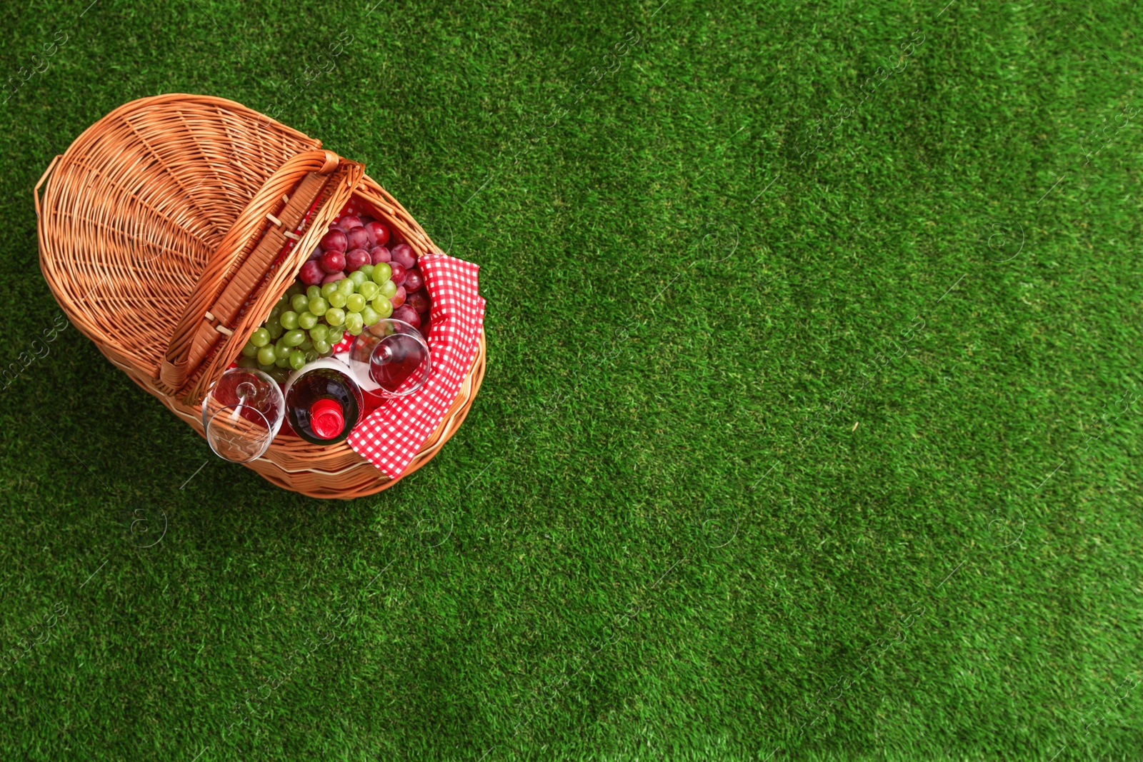 Photo of Picnic basket with wine and grapes on grass, top view. Space for text