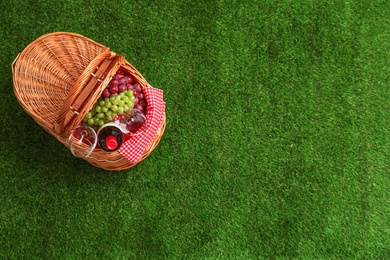 Picnic basket with wine and grapes on grass, top view. Space for text