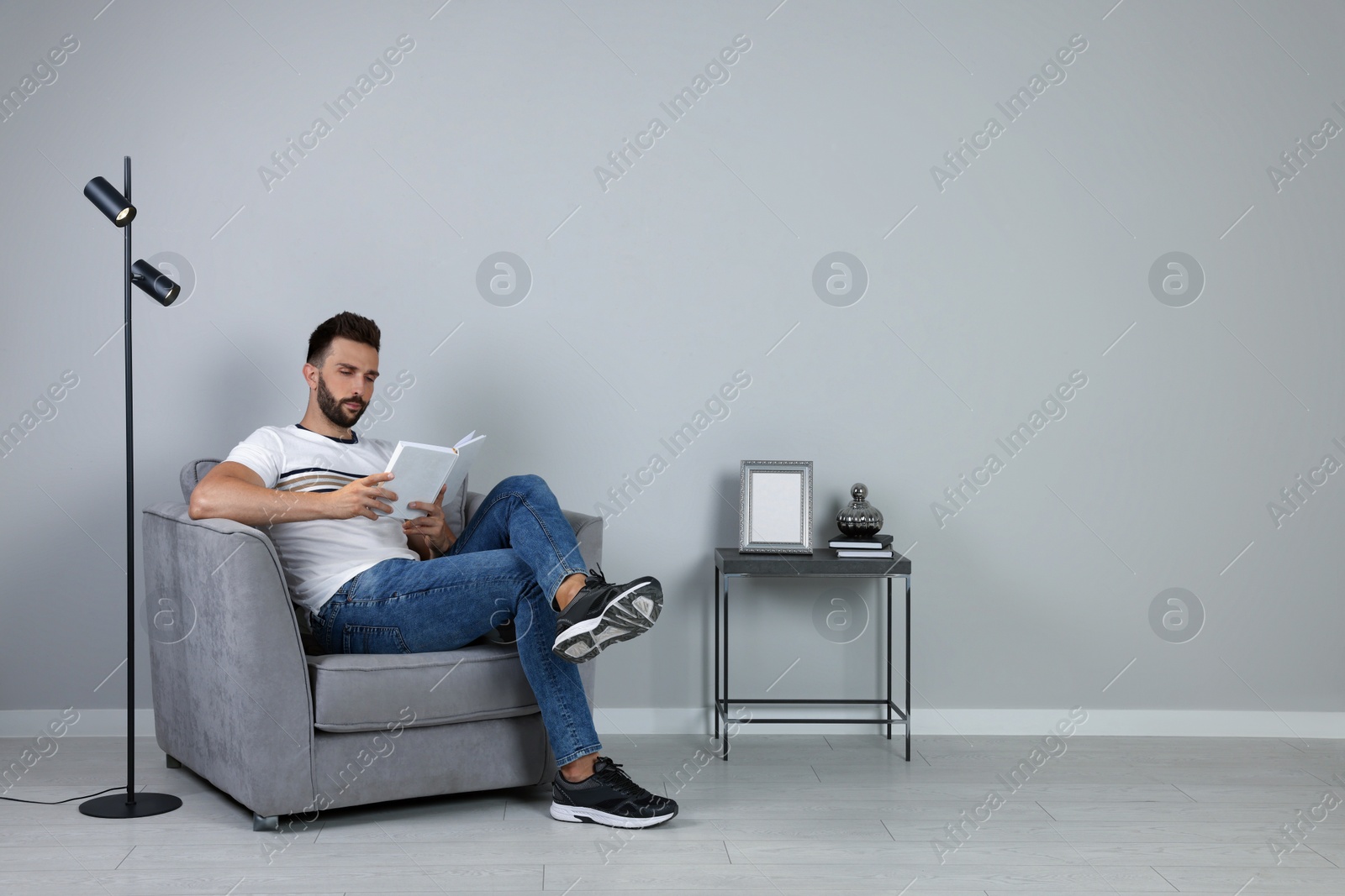 Photo of Man reading book in armchair near gray wall, space for text