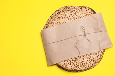 Photo of Top view of tasty matzos wrapped with paper on yellow background, space for text. Passover (Pesach) celebration