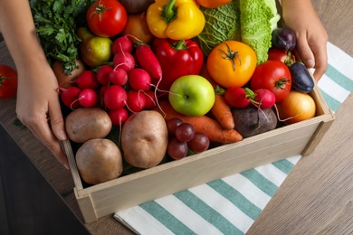 Photo of Farmer with crate full of different vegetables and fruits at wooden table, closeup. Harvesting time