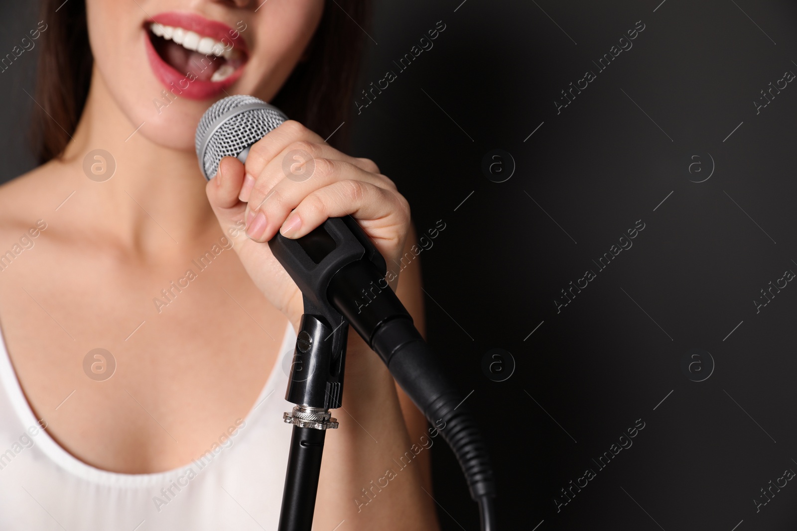 Photo of Young woman singing in microphone on dark background, closeup view with space for text