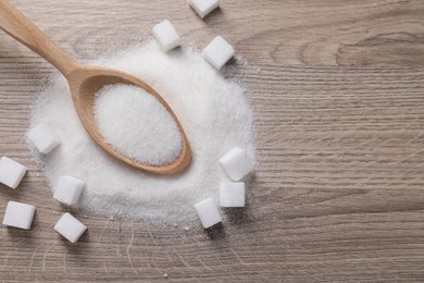 Photo of Different types of white sugar and spoon on wooden table, top view. Space for text