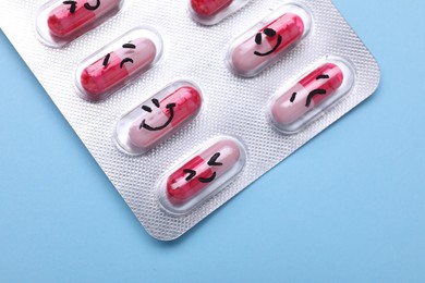 Photo of Blister of antidepressant pills with emotional faces on light blue background, top view