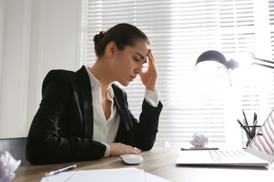 Stressed and tired young woman with headache at workplace