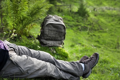 Photo of Woman with backpack sitting on green grass, closeup. Summer camping