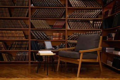 Photo of Cozy home library interior with comfortable armchair, laptop and collection of vintage books on shelves