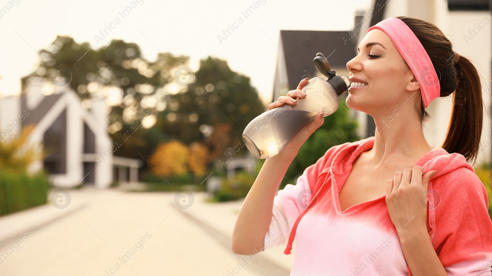 Photo of Beautiful sporty woman drinking water after running on street. Healthy lifestyle