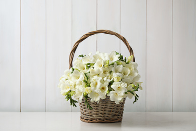 Photo of Beautiful freesia flowers in basket on white table