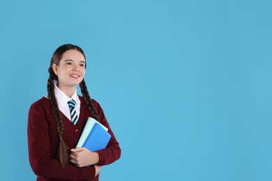 Photo of Teenage girl in school uniform with books on light blue background, space for text
