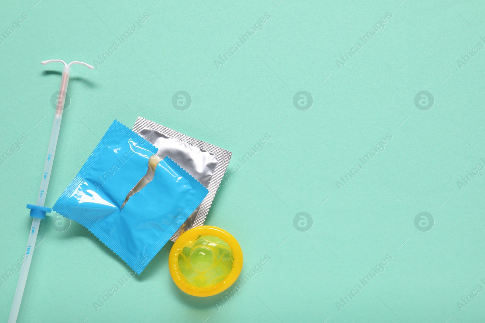 Photo of Condoms and intrauterine device on turquoise background, flat lay and space for text. Choosing method of contraception