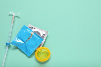 Photo of Condoms and intrauterine device on turquoise background, flat lay and space for text. Choosing method of contraception