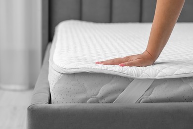 Photo of Woman touching new soft mattress on grey bed indoors, closeup