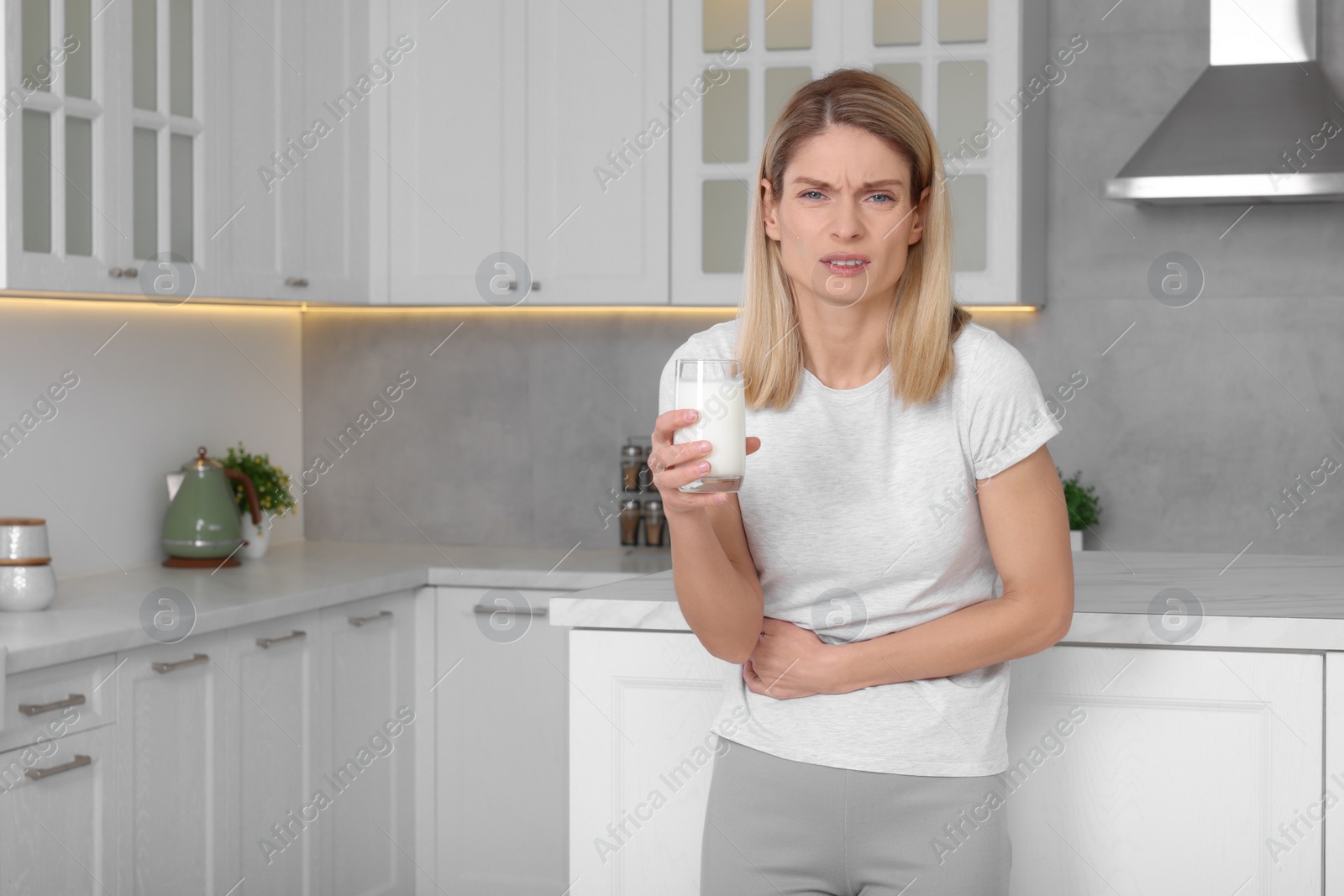 Photo of Woman with glass of milk suffering from lactose intolerance in kitchen, space for text