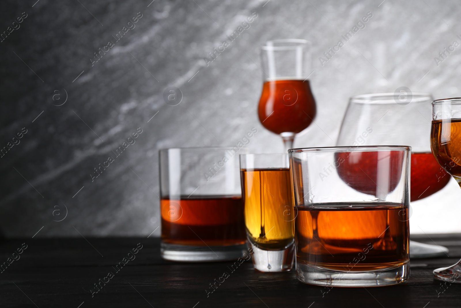 Photo of Different delicious liqueurs in glasses on dark wooden table, space for text