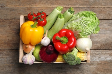 Photo of Fresh vegetables in crate on wooden table, top view