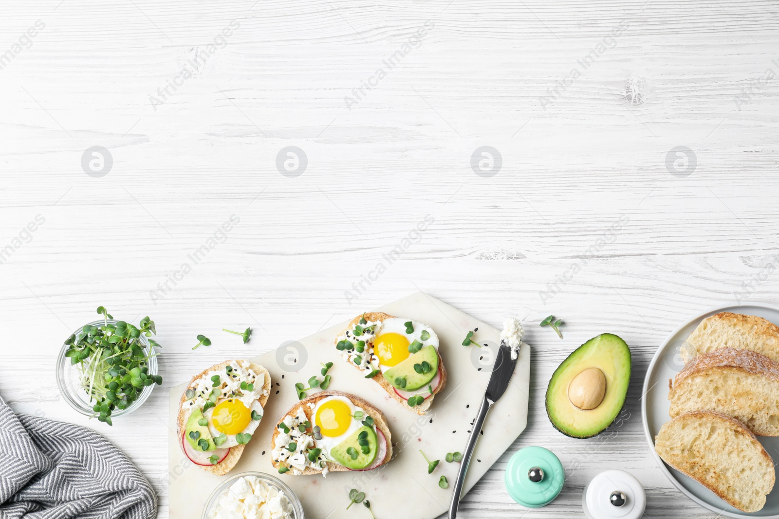 Photo of Delicious sandwiches with egg, cheese, avocado and microgreens on white wooden table, flat lay. Space for text