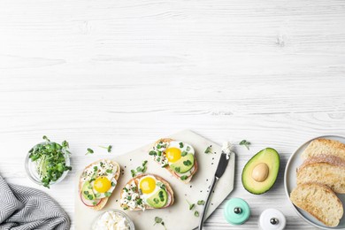 Delicious sandwiches with egg, cheese, avocado and microgreens on white wooden table, flat lay. Space for text
