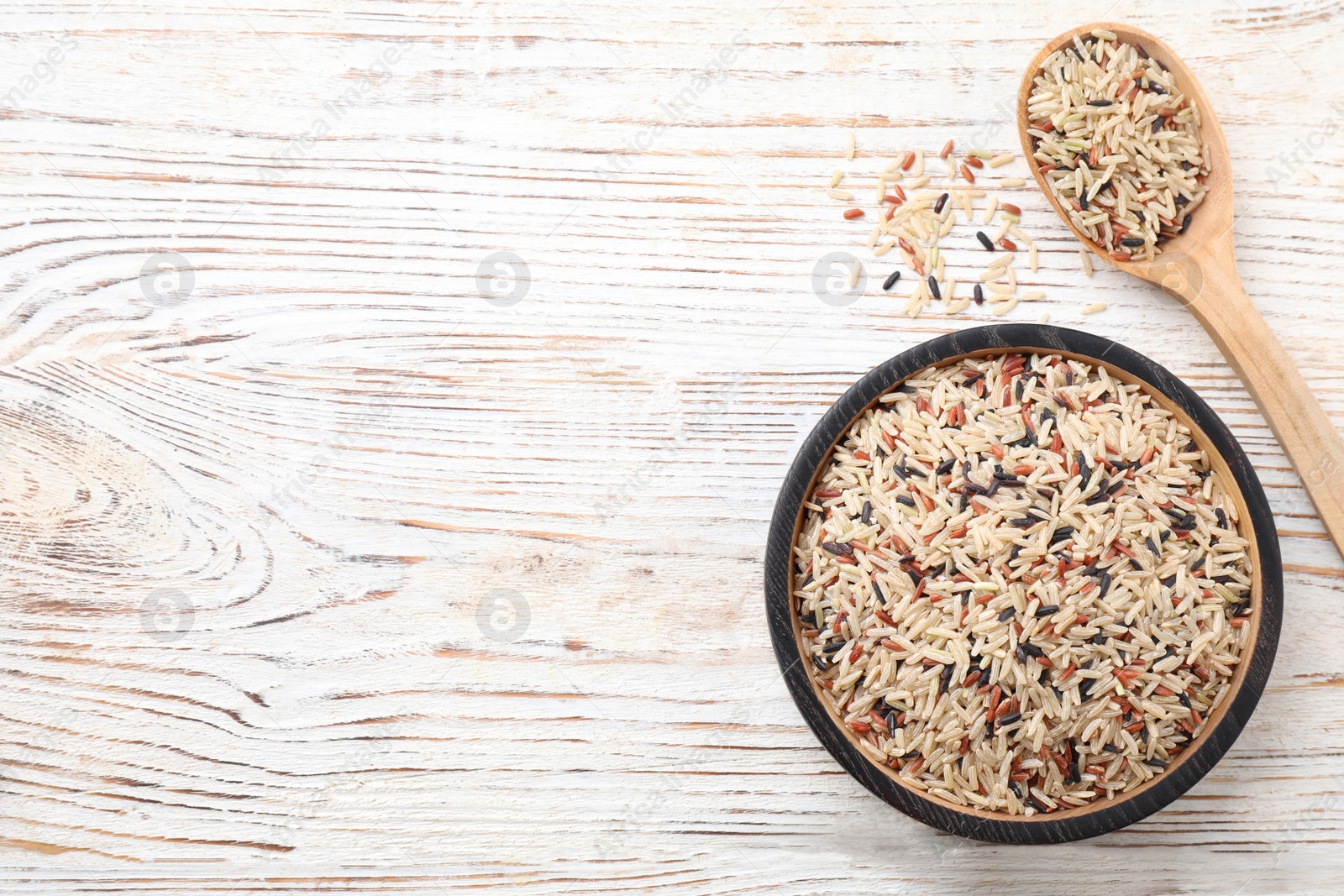 Photo of Mix of different brown rice on white wooden table, flat lay. Space for text