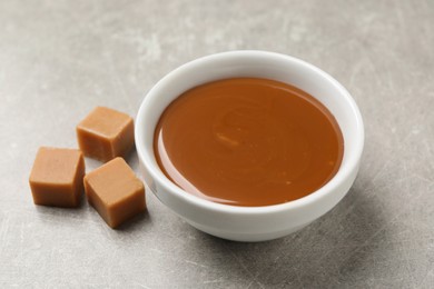 Photo of Yummy salted caramel in bowl and candies on grey table