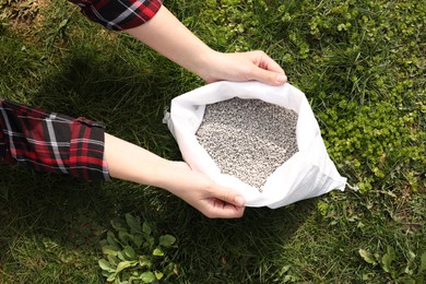 Woman with bag of fertilizer on green grass outdoors, top view