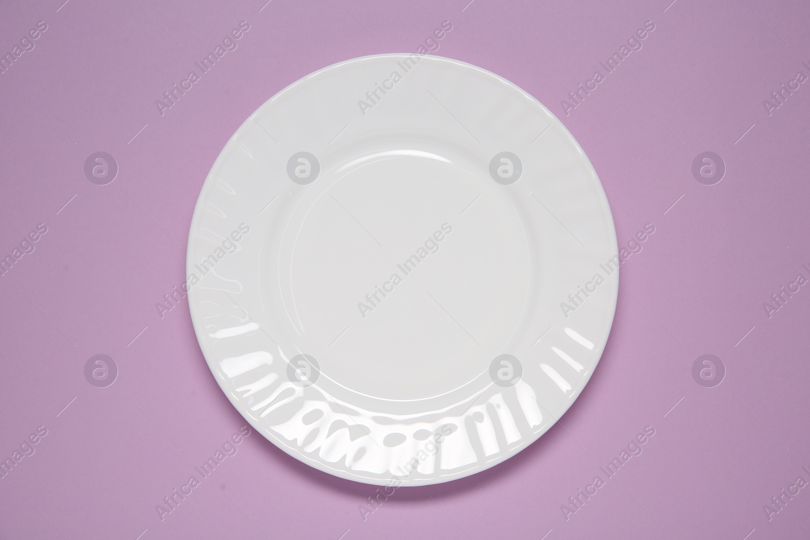 Photo of One white plate on violet background, top view