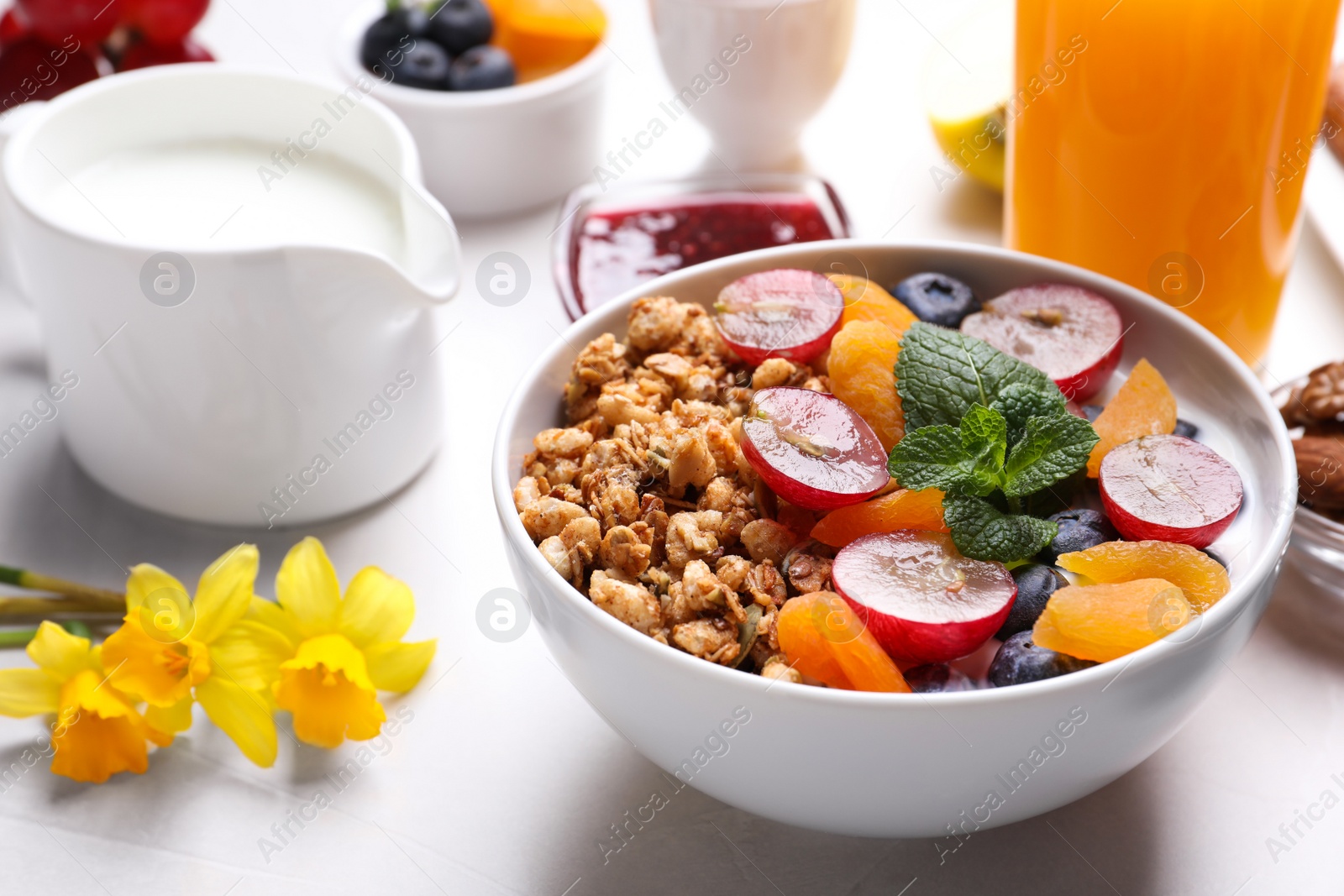 Photo of Delicious granola with fruits on white table, closeup