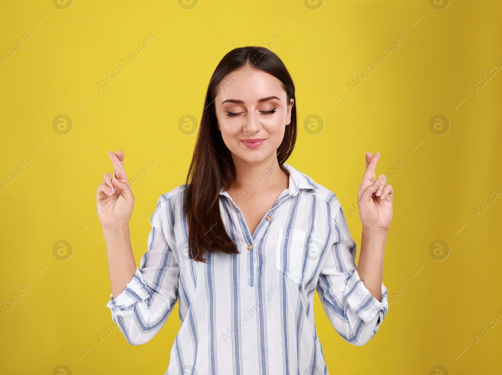 Photo of Beautiful young woman in casual outfit  crossing her fingers on yellow background