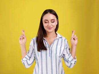 Beautiful young woman in casual outfit  crossing her fingers on yellow background