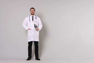 Photo of Full length portrait of smiling doctor with tablet on light grey background, space for text