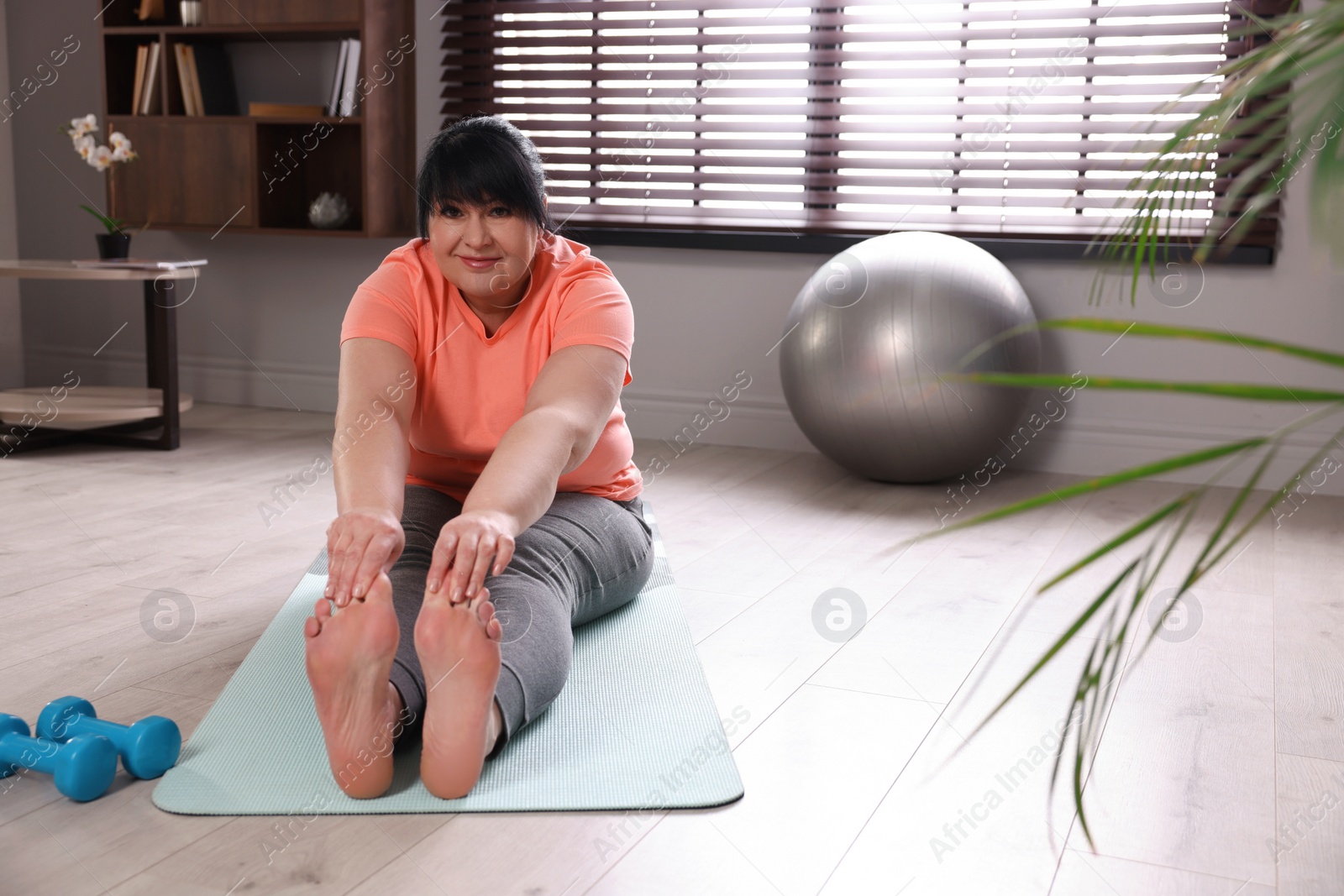 Photo of Overweight mature woman stretching on yoga mat at home, space for text