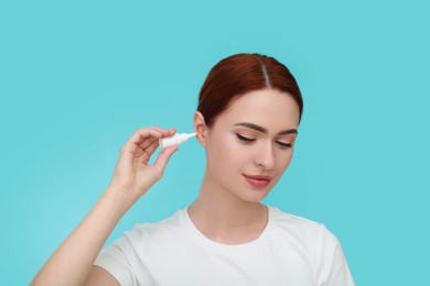 Woman using ear drops on light blue background