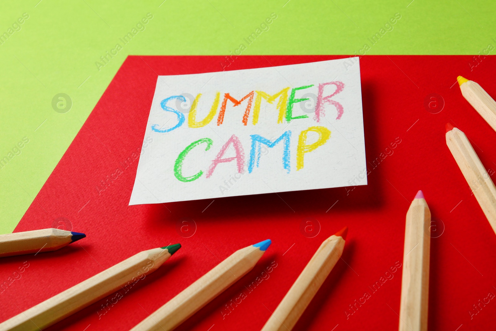 Photo of Paper with written text SUMMER CAMP and different pencils on color background