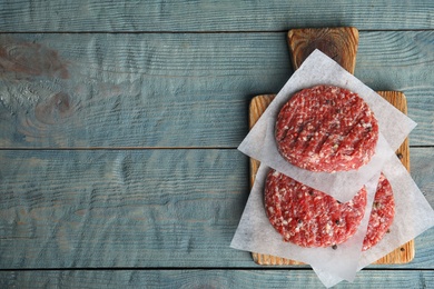 Raw meat cutlets for burger on blue wooden table, top view. Space for text