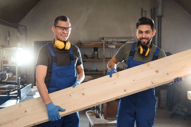 Photo of Professional carpenters with large wooden board in workshop	