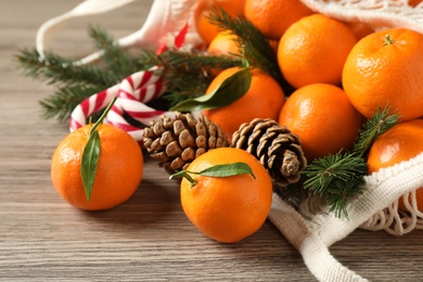 Photo of Fresh tangerines, Christmas candy canes, fir tree branches and cones in mesh bag on wooden table, closeup