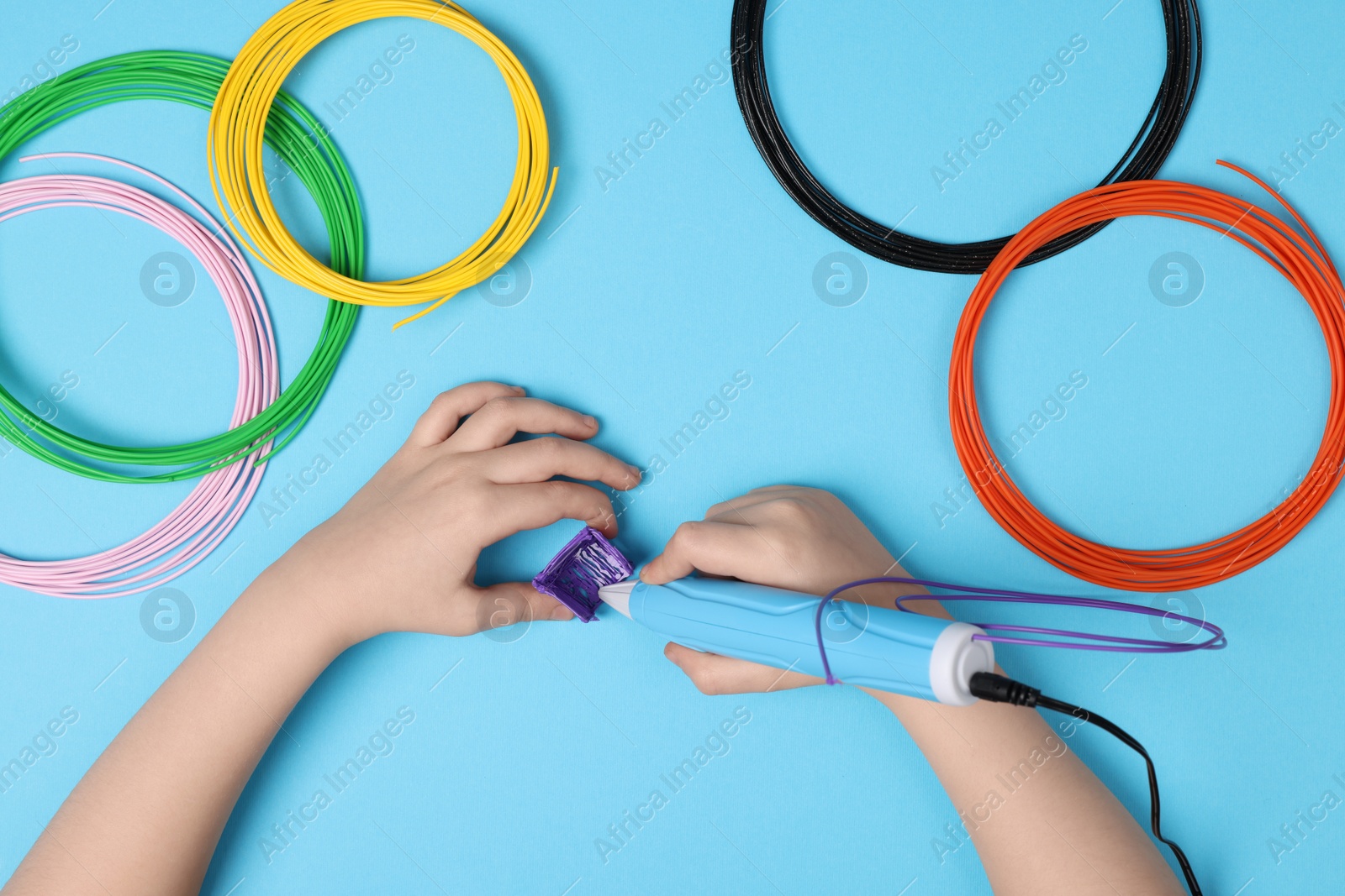 Photo of Boy drawing with stylish 3D pen on light blue background, top view