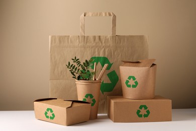 Image of Set of eco friendly food packaging with recycling symbols on white table against beige background