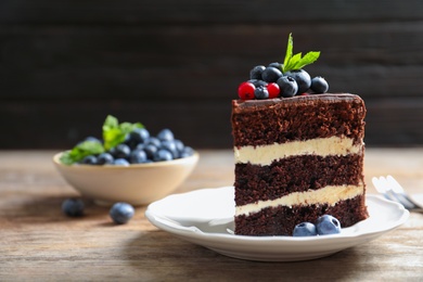 Plate with slice of chocolate sponge berry cake on wooden table