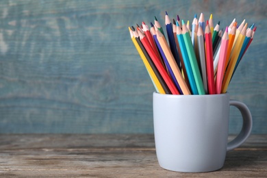 Photo of Colorful pencils in cup on wooden table. Space for text