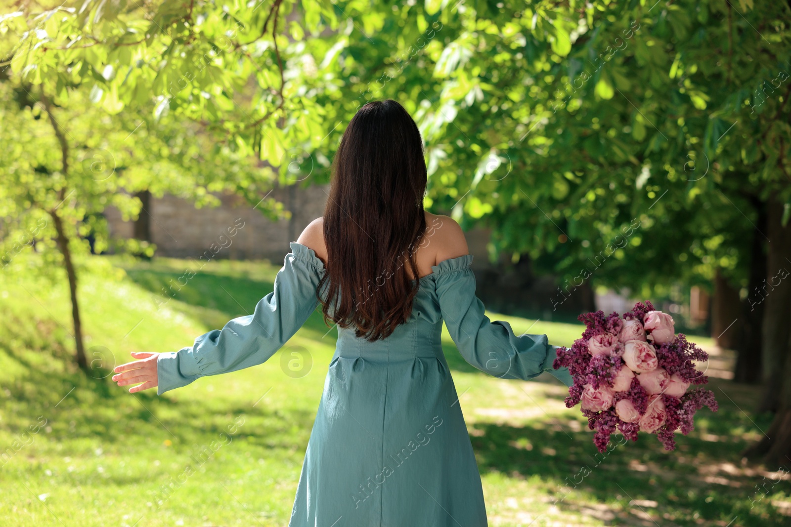 Photo of Woman with bouquet of spring flowers in park on sunny day, back view