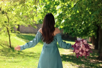 Photo of Woman with bouquet of spring flowers in park on sunny day, back view