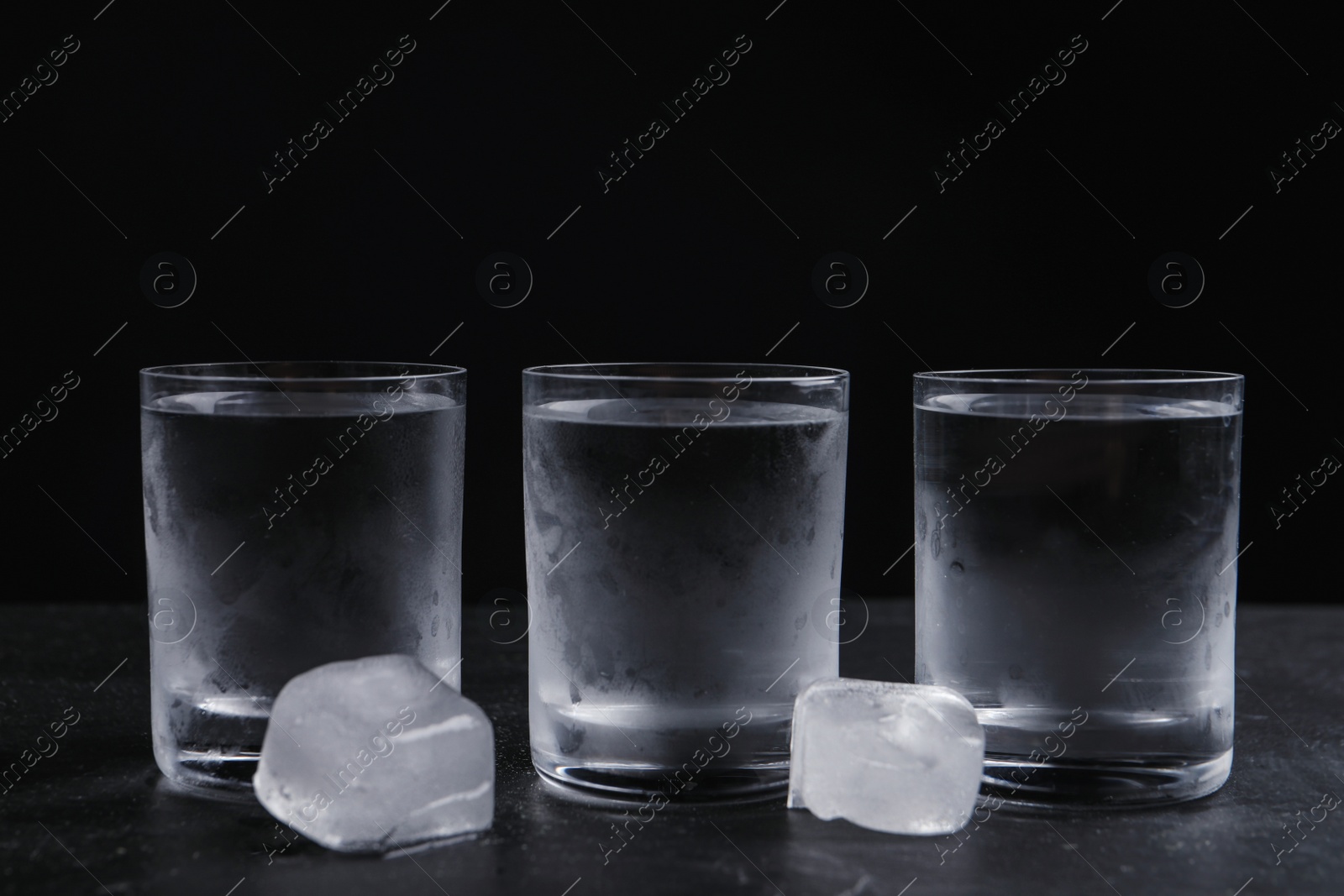 Photo of Vodka in shot glasses with ice on table against black background