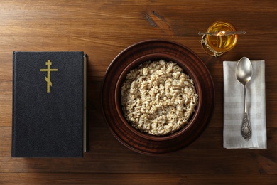 Bible, oatmeal porridge and spoon on wooden table, flat lay. Lent season