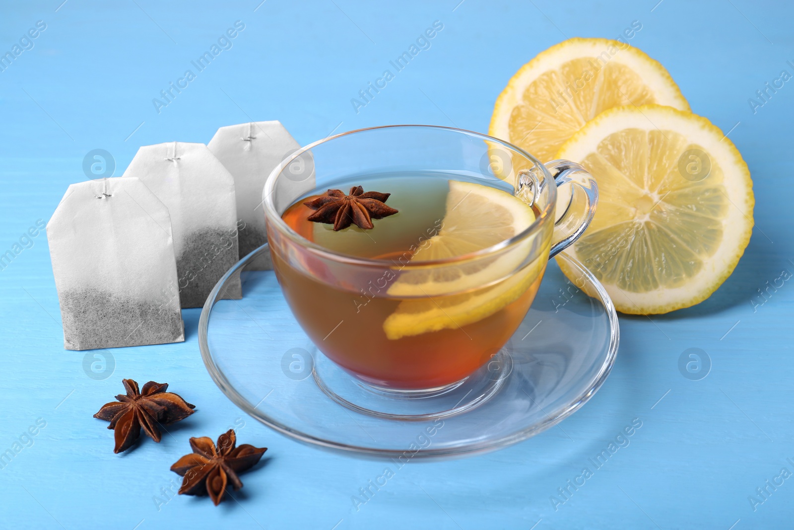 Photo of Tea bags, cup of hot drink, anise stars and lemon on light blue wooden table