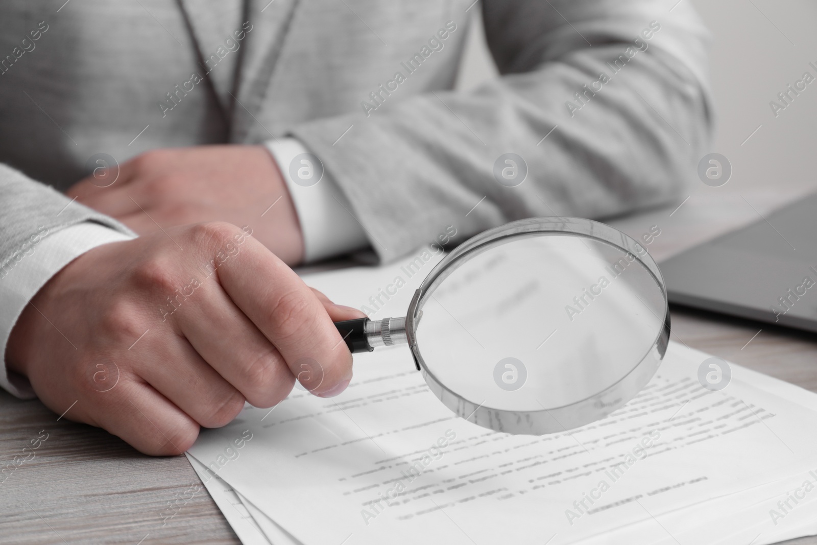 Photo of Man looking at document through magnifier at white wooden table, closeup. Searching concept