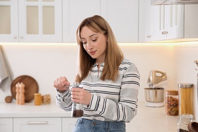 Photo of Young woman using manual coffee grinder in kitchen